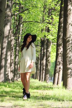 Beautiful young woman in hat walking in spring alley