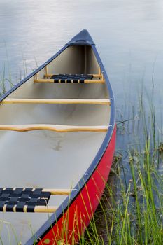 red canoe on a calm lake with a green grass - summer paddling concept