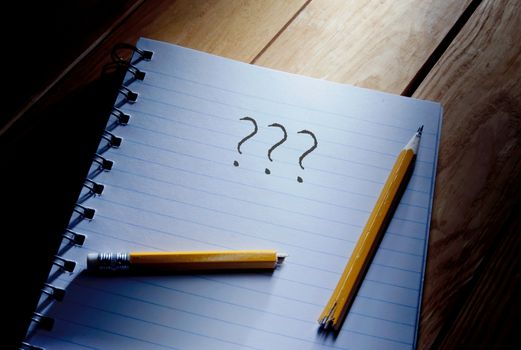 Three questions mark and broken pencil on top of a note pad 