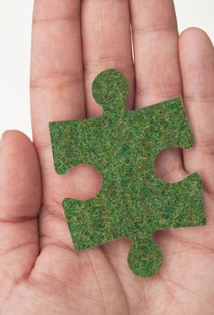 Hand holding a grass covered jigsaw puzzle piece 