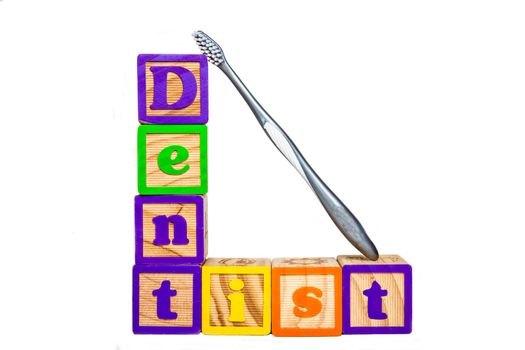 This is a photograph of blocks spelling the word dentist and a toothbrush leaning against them.