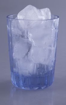 Glass with ice cubes over gray background