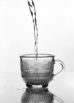 cup glass with water pouring on glass table (gray scale)
