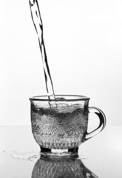 cup glass with water pouring on glass table (gray scale)