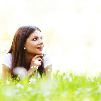 Pretty brunette girl laying on grass with white  flowers around her