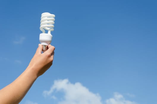 hand holding energy saving lamp on blue sky background