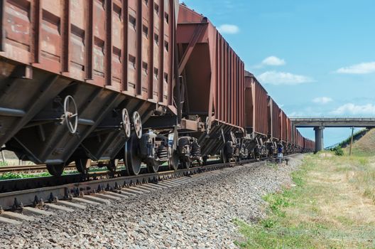 wagons of a freight train in motion go to horizon under bridge