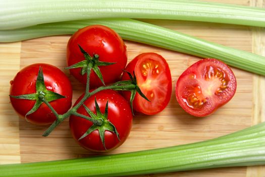 High angle view of bunch of fresh tomatoes and celery sticks on wooden chopping board 