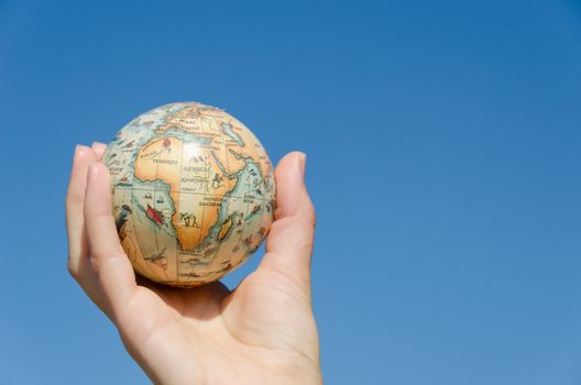 earth globe miniature model in female palm on blue sky background, Africa, symbolizing environmental care.