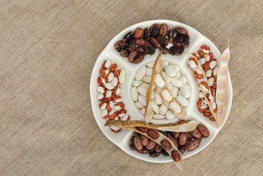 dried colorful winter beans mix in white plate on linen texture background
