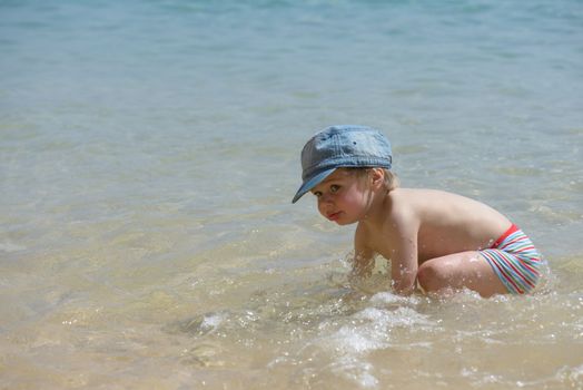 Little boy in denim hat playing in the sea