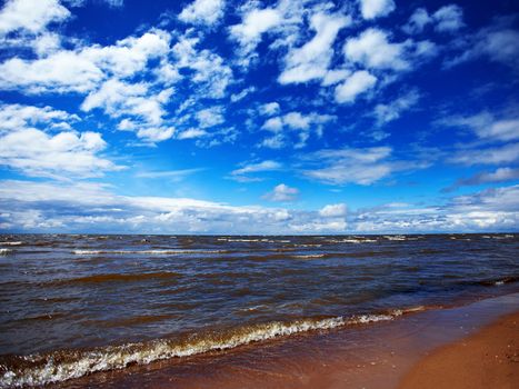 The sky with clouds and a beach. Landscape with the lake. Sunny day on the lake. Beautiful landscape. Sandy beach and waves.