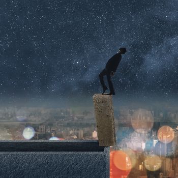 Concept of dangerous balance, business man dancing on a stone of the roof of city under stars in night.