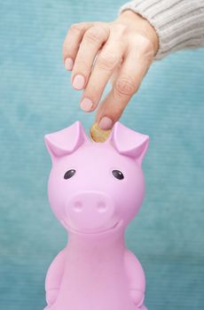 A hand dropping a euro coin into a pink piggy bank saving box