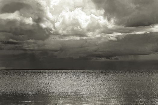 Black and white hdr landscape of a dark, dramatic lake with Moon behind clouds.