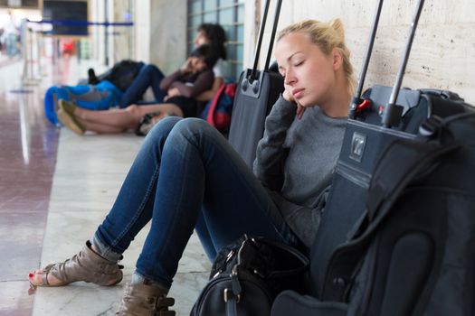 Tired female traveler waiting for departure, resting on the station floor with all her luggage.