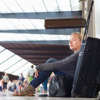 Tired female traveler waiting for departure, sitting on the station floor with all her luggage.