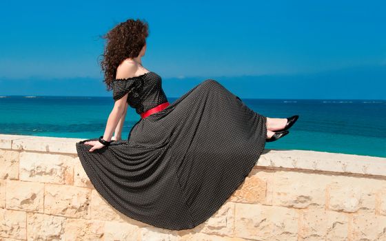 Girl sitting on the parapet in a beautiful long dress and posing for a photograph