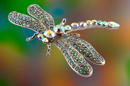 Jewellery with colored stones in the shape of a dragonfly against a yellow and green background