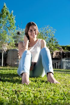 Portrait of cheerful girl ripped jeans sitting on the grass in the park against the rocks