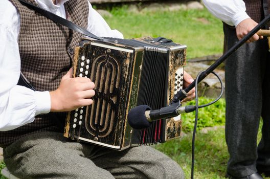 Accordionist young man in traditional clothes play folk music with accordion in rural party.