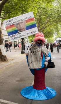 BERLIN, GERMANY - JUNE 21, 2014: Christopher Street Day.Crowd of people Participate in the parade celebrates gays, lesbians, bisexuals and transgenders.Prominent in the image a Elaborately dressed participant holds a placard with a slogan over the face of Russian President Vladimir Putin.