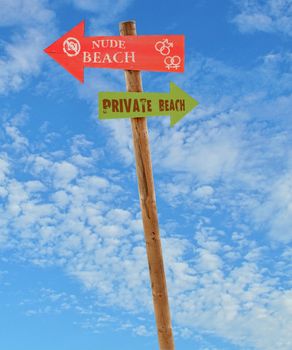 wooden arrow direction signs post to the nude and private beaches against a blue sky