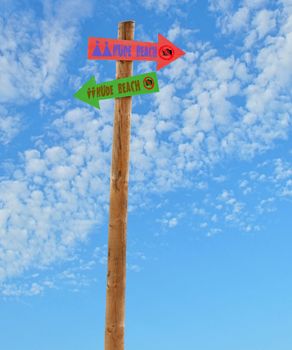 wooden arrow direction signs post to the nude female and male beaches against a blue sky