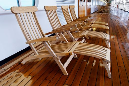 Diminishing view of a row of deck chairs on a cruise ship with a wet teak wood floor