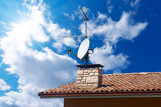 Satellite dish and TV antennas on the house roof with a beautiful blue sky