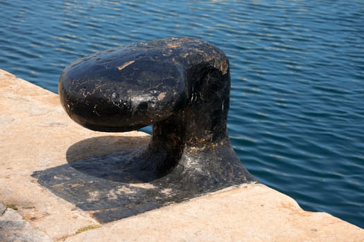 Detail of old and black mooring bollard on the pier with water in the background