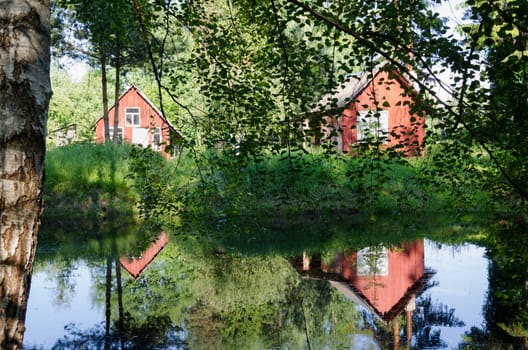 two small red rural home reflected through birch branches on pond