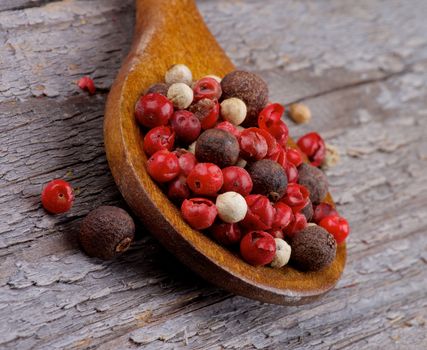 Mixed Red, Black and White Peppercorn in Wooden Spoon closeup on Rustic Wooden background