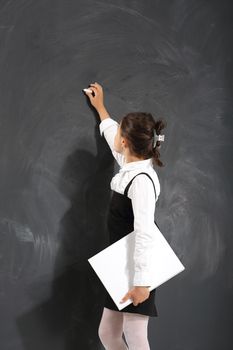 Schoolgirl holding heavy books standing on a background of black wall