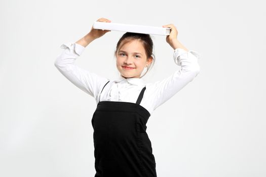 Girl in school uniform on a white background with books on her head