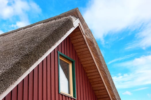 roof of a thatched-roof house, blue cloudy sky in the background