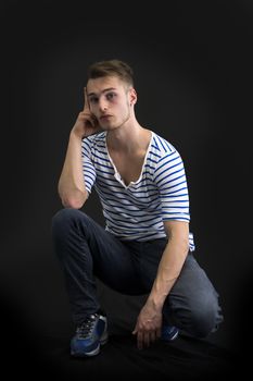 Handsome blond young man sitting on black background looking at camera