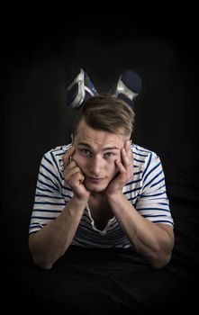 Handsome blond young man laying on black background looking at camera