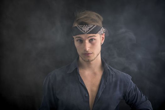Handsome blond young man wearing bandana, smoke around him, dark background