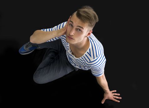 Handsome blond young man sitting on black background looking at camera, shot from above