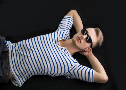 Cool blond young man laying on the floor with sunglasses on, hands under his head