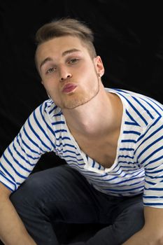 Handsome young man sending a kiss with his lips towards camera, isolated on black