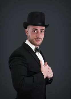 Attractive young businessman with suit, top-hat and bowtie on dark background