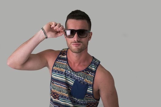 Cool confident young man with sunglasses and tank-top on light grey background