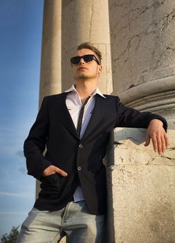 Handsome blond young man with marble columns behind him, looking away