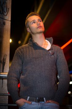Handsome blond young man alone in urban setting, looking away, night shot