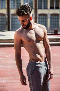 Handsome shirtless young man with beard looking down to a side