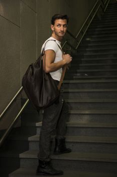 Handsome young man standing with big bag on stairs' steps, looking away