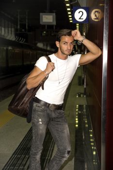 Handsome young man standing against wall in train or subway station, looking at camera