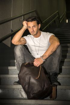 Handsome young man sitting on stairs' granite steps, looking at camera